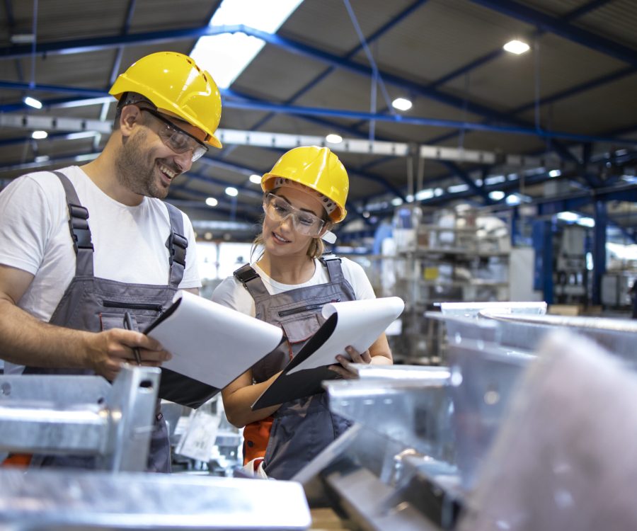 Factory workers analyzing production results in large industrial hall.